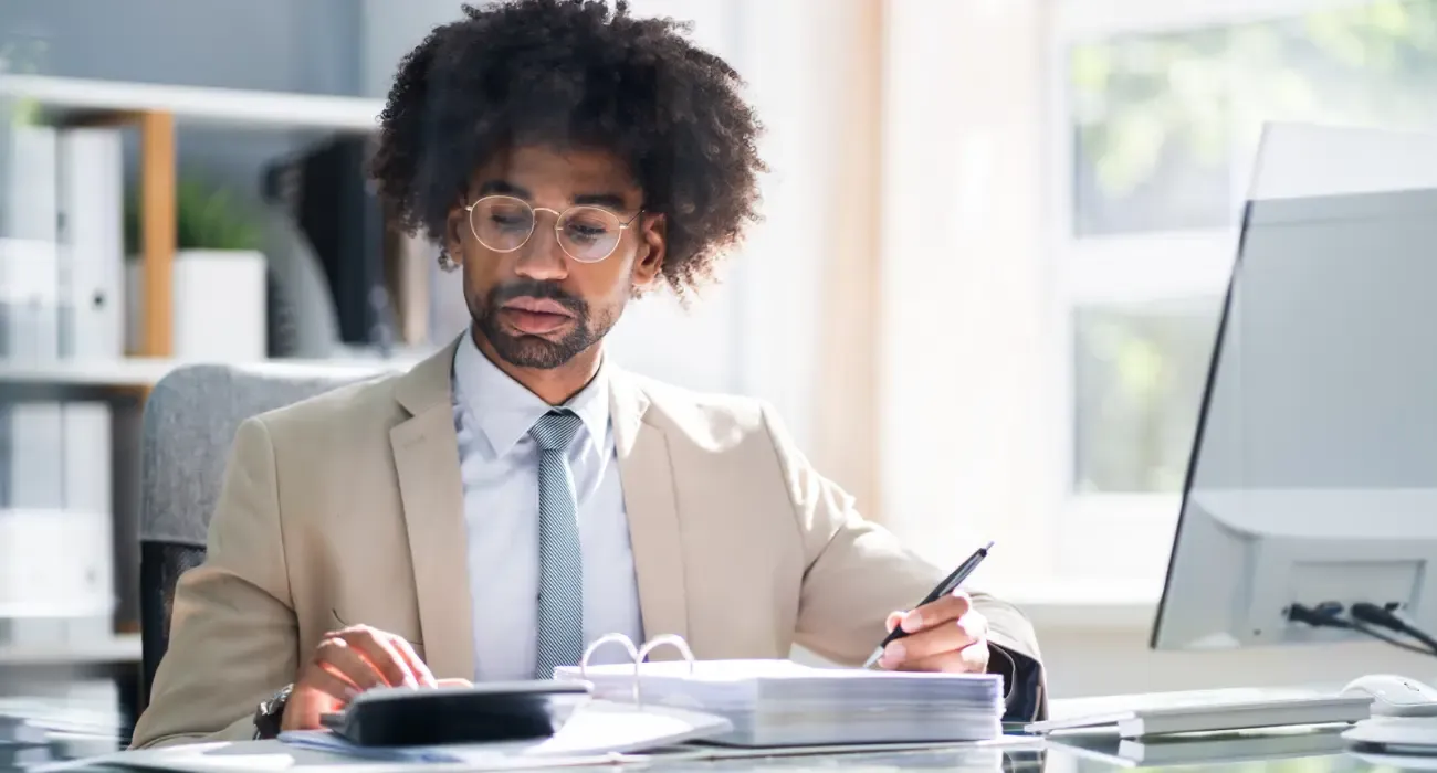An accountant reviewing paperwork with a calculator at an office desk