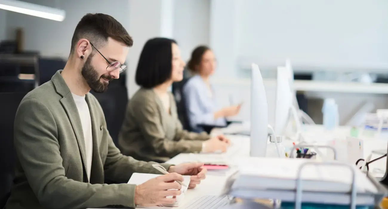 A creative team working side by side at a shared desk in an open-plan studio